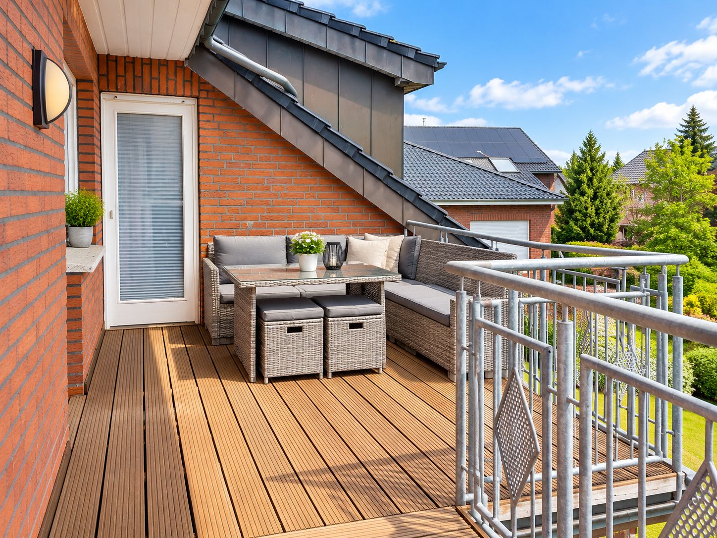 Eine Holzterrasse mit Gartenmöbeln, einer Ziegelwand und einem Metallgeländer.