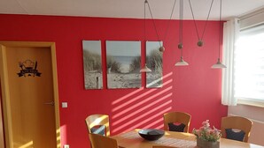 A dining area with a wooden table, chairs, and a red wall with three framed pictures. - Comfortable accommodation in a cozy atmosphere for you and your dog. (Neuenkirchen)