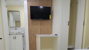 A hotel room with a large bed, a TV mounted on the wall, a mirror, and a wardrobe.