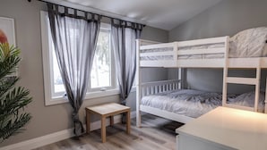 Habitación con literas, una pequeña mesa, una ventana con cortinas y una planta.
