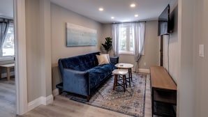 Una sala de estar moderna con un sofá de terciopelo azul, una mesita redonda y un televisor montado en la pared.