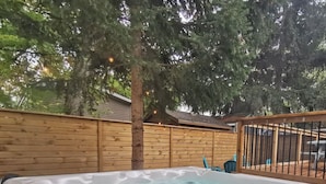 Un jacuzzi en un patio trasero con una valla de madera y un árbol.