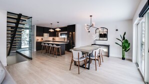 Una cocina moderna con una isla central, taburetes de bar, iluminación colgante y una escalera que sube a un nivel superior.