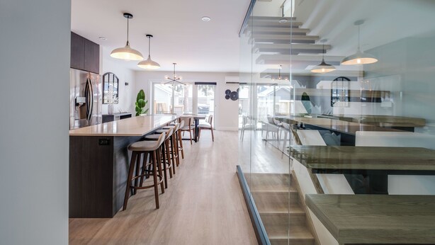 Una cocina moderna con una isla central, taburetes de bar, iluminación colgante y una escalera que conduce a un nivel superior.
