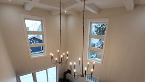 Amplia sala de estar con una gran lámpara de araña, chimenea y varios ventanales con vistas al exterior.
