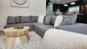 Una sala de estar moderna con un sofá seccional gris, una mesa de centro redonda de madera y una alfombra estampada.