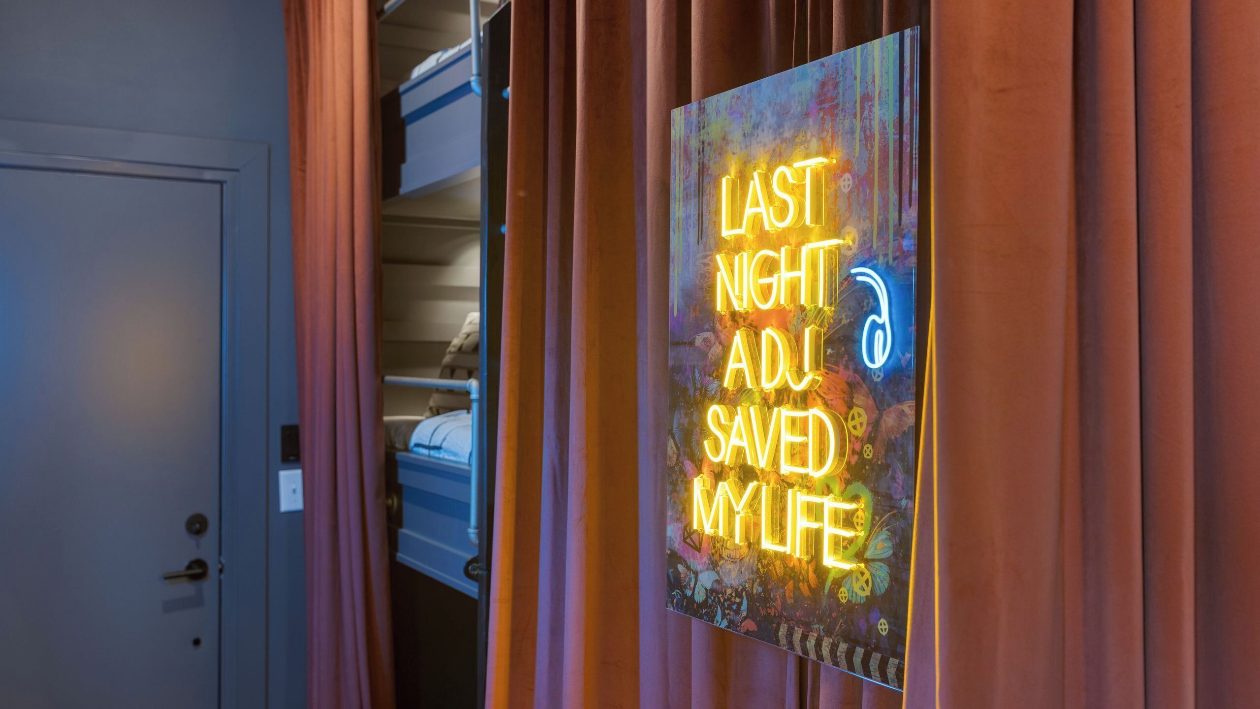 A room with a bed, a door, and a neon sign on the wall.