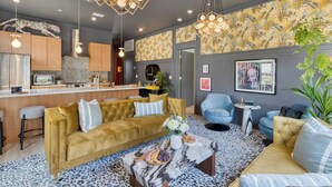 A modern living room with a sofa, coffee table, and chairs. There is a kitchen area with cabinets and a countertop. - Colorful 4BR w/ Artful Design, Dining & Easy Access to Broadway The Bloom House by Avantstay (Nashville)
