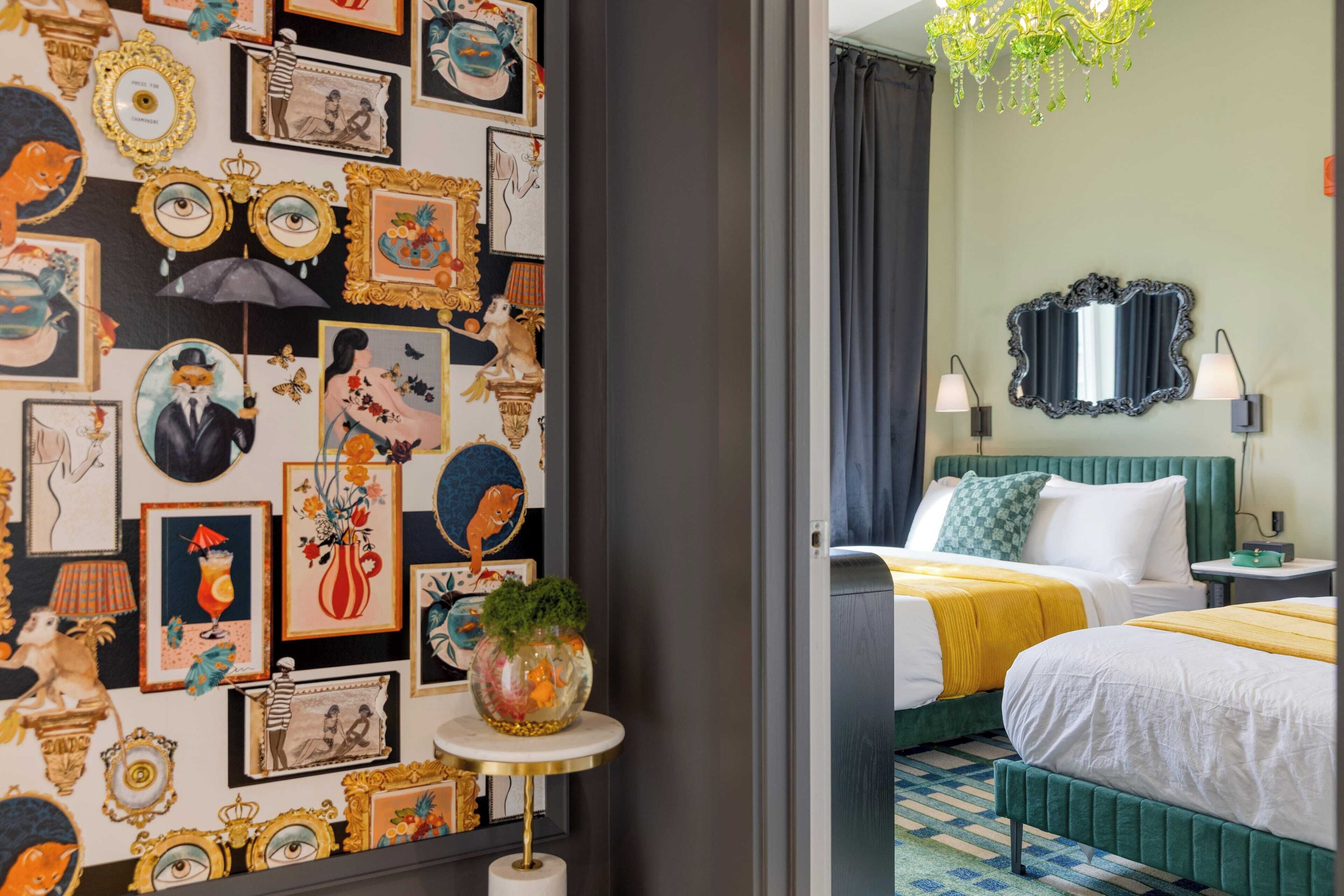 A hotel room with a wall decorated with various framed artworks, a round table with a vase, and a bed with green bedding.