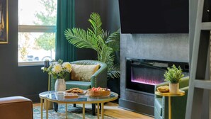 A cozy living room with a green armchair, a round glass coffee table, a fireplace, and a potted plant. - Stylish Studio Near Broadway & East Nashville Restaurants Lischey Loft by Avantstay (Nashville)