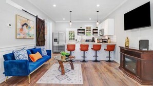 Un salon moderne avec un canapé bleu, une table basse et un coin cuisine comprenant un bar et des tabourets.