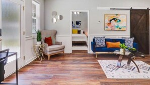 Un salon spacieux doté d’un plancher en bois, d’un canapé bleu, d’un ventilateur de plafond et d’un coin repas avec une table et des chaises.