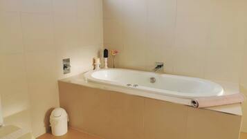 A bathroom with a bathtub, toilet, and a trash bin.