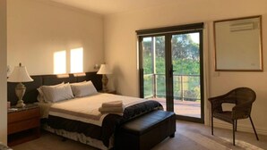 Un dormitorio con cama, lámparas de noche, una silla y un ventanal corredero que da a un espacio exterior.