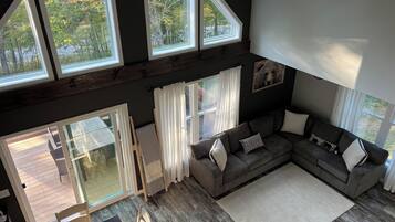A modern living room with a large gray sectional sofa, a dining table with chairs, and a view of a deck through large windows.