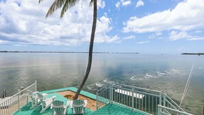 Varanda com cadeiras e palmeira com vista para águas calmas.