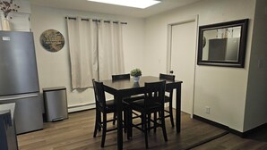 A compact kitchen with a dining area, a refrigerator, a trash bin, and a wall-mounted mirror.