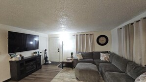 A living room with a flat-screen TV, a sofa, a coffee table, and a rug.
