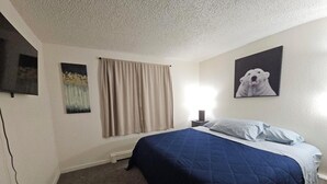 A bedroom with a bed, a nightstand, a lamp, a painting of a dog, and a window with curtains.