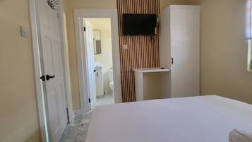 Une chambre d’hôtel avec un lit, un téléviseur fixé au mur, une petite table et une fenêtre avec des stores.
