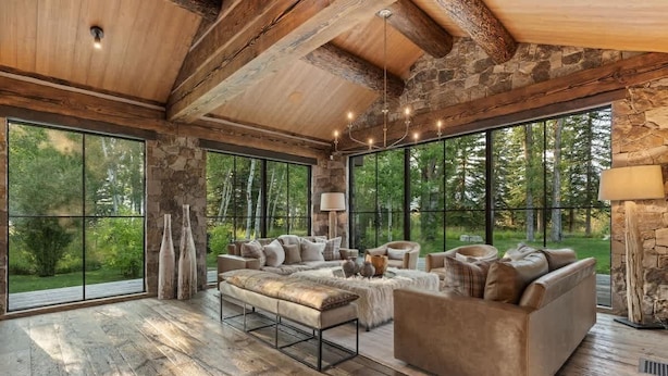 A spacious living room with a large sofa, a coffee table, and a fireplace. There are large windows offering a view of the outdoors. - Abode at Teton Game, sweeping estate with 3 cabins (Wilson)
