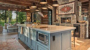 A spacious kitchen with a large island, stone fireplace, and modern lighting fixtures. - Abode at Teton Game, sweeping estate with 3 cabins (Wilson)