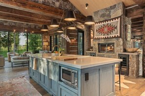 Una cocina amplia con una isla grande, chimenea de piedra e iluminación moderna.