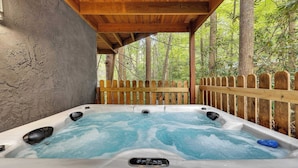 Un bain à remous situé dans une zone boisée, avec une terrasse en bois et une clôture en bois.