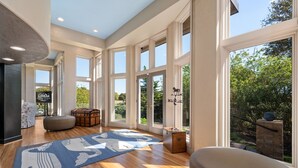 A spacious room with large windows, a wooden floor, and a blue rug with a white pattern.