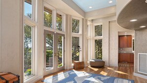 A spacious room with large windows, a wooden floor, and a blue patterned rug.