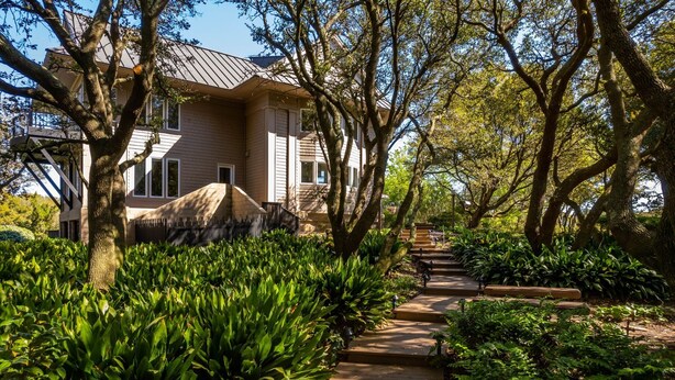 A house with a pathway leading to the entrance, surrounded by lush greenery and trees.