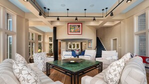 A spacious living area with a high ceiling, large windows, and a central coffee table.