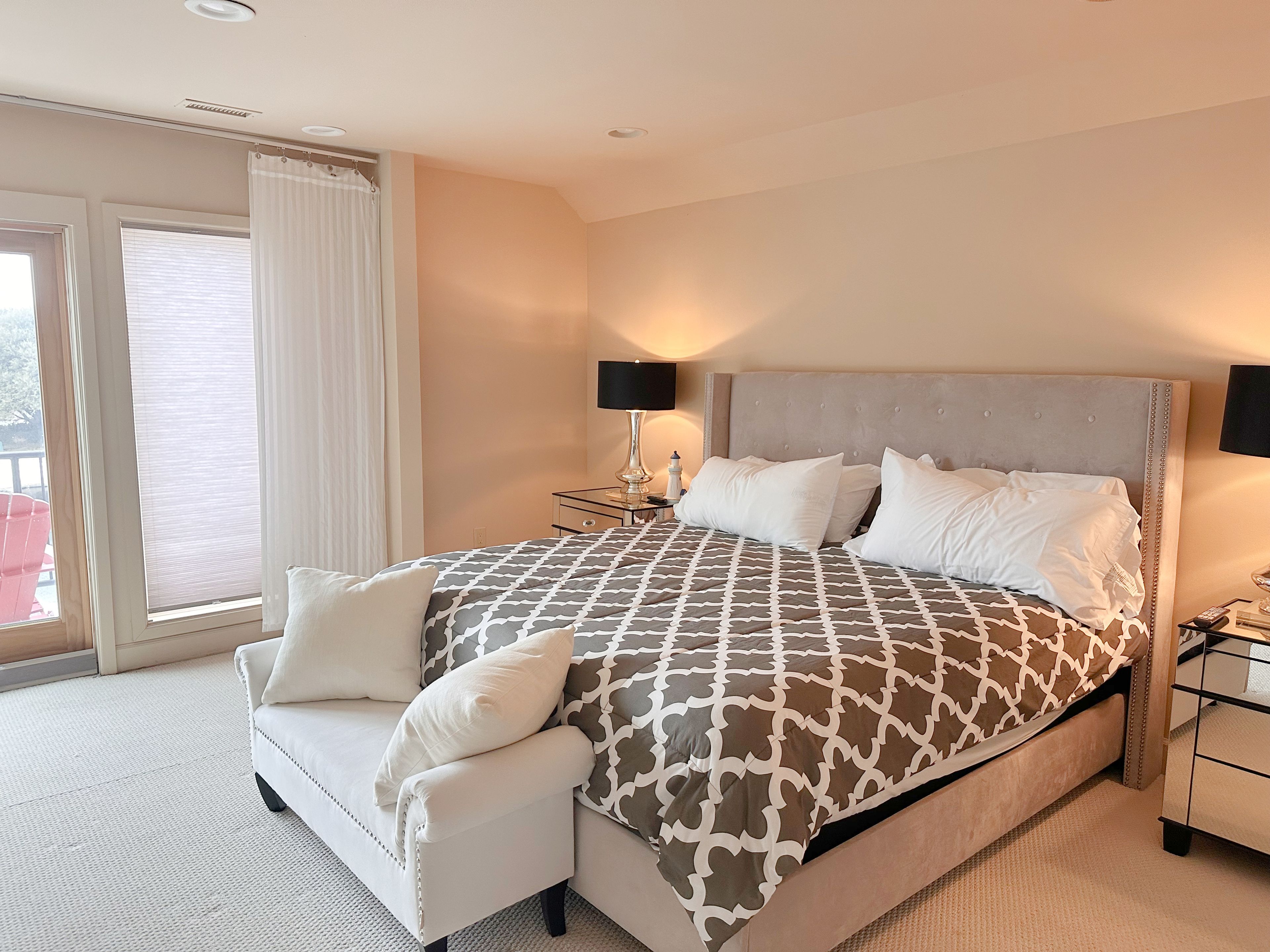 Ein Hotelzimmer mit einem großen Bett, einer Couch, einem Nachttisch, einer Lampe und Blick ins Freie.