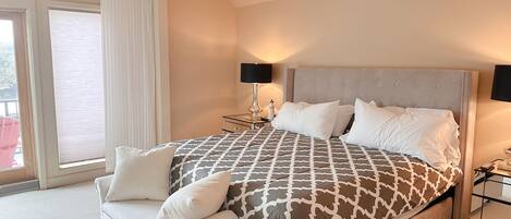 Ein Hotelzimmer mit einem großen Bett, einer Couch, einem Nachttisch, einer Lampe und Blick ins Freie.