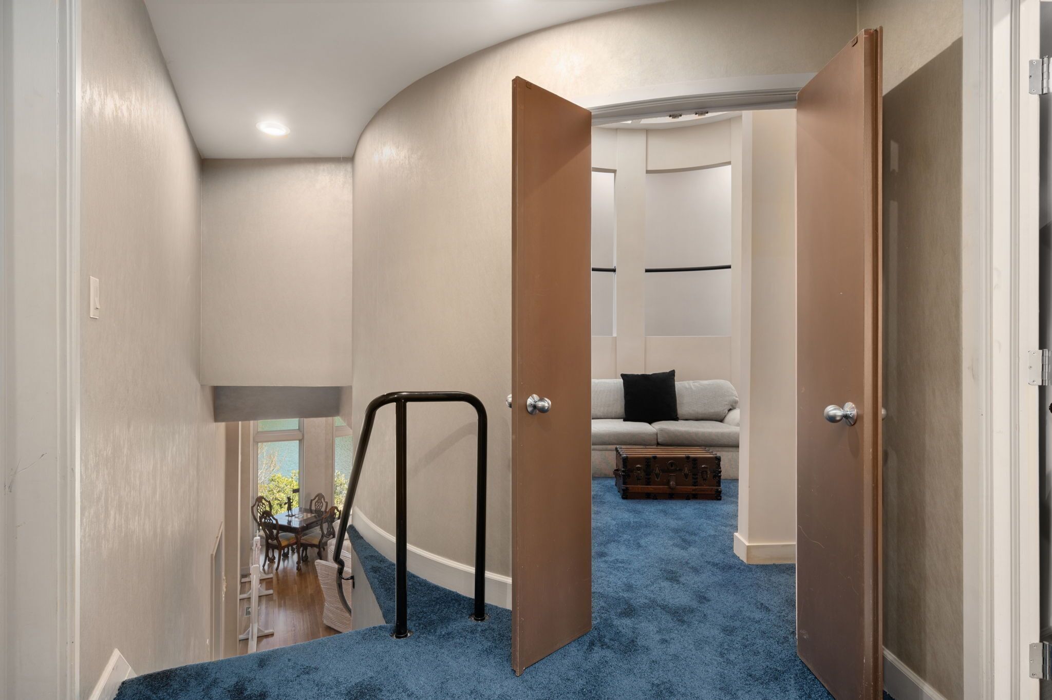 Un couloir avec un tapis bleu qui mène à un coin repas comprenant une table et des chaises, un canapé blanc et une commode.