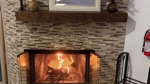 A fireplace with a stone wall backdrop, a framed picture above it, and a small shelf with decorative items.