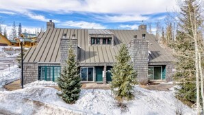 A modern two-story house with a sloped roof, stone chimneys, and a garage.