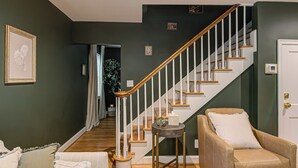 Una escalera con escalones de madera y barandillas blancas, un sillón color beige con un cojín blanco y una pequeña mesa redonda con una planta y una vela.