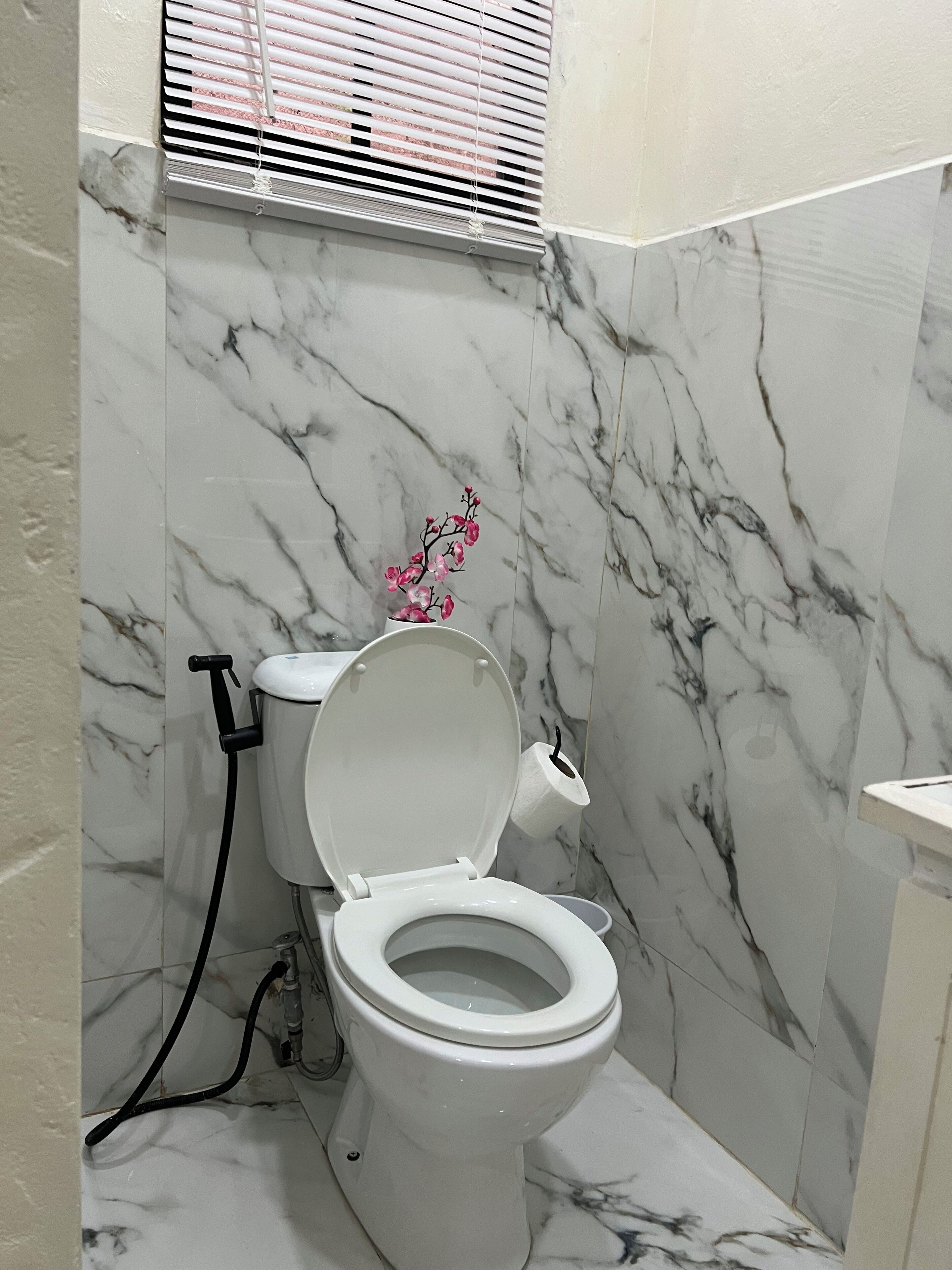 A bathroom with a toilet, marble walls, and a window with blinds.