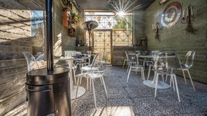 An outdoor dining area with clear chairs, a large metal grill, and a brick wall.