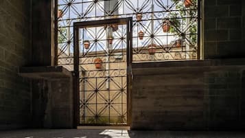 Ein mit geometrischen Mustern gefliester Boden, ein Metallgitter mit Verzierungen und ein Blick auf ein Gebäude mit Terrakotta-Dachziegeln durch das Gitter hindurch.
