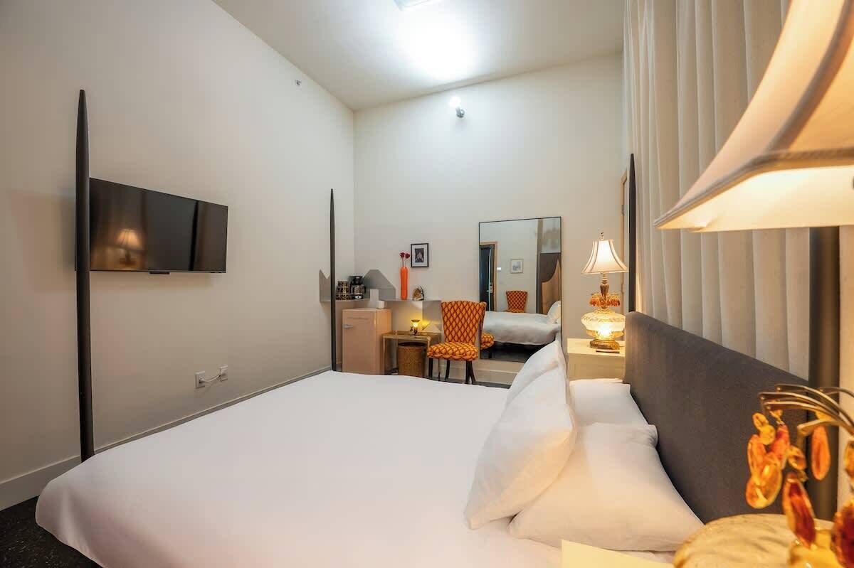 Hotellihuone, jossa on suuri sänky, seinälle asennettu taulutelevisio, työpöytä tuolilla, peili ja lamppu.