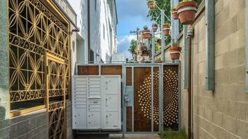 Une ruelle étroite, avec un bâtiment blanc sur la gauche, une porte en métal et un local de stockage blanc.