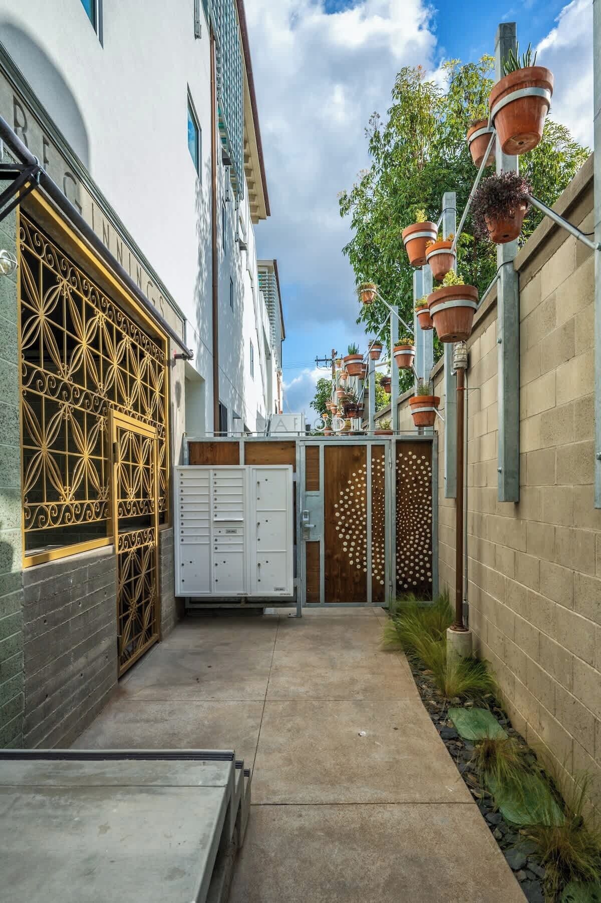 Un callejón estrecho con un edificio blanco a la izquierda, una reja metálica y un contenedor blanco.