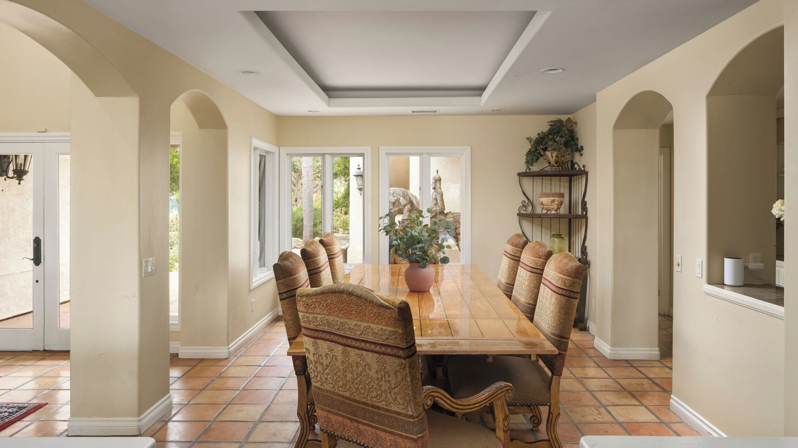 A dining room with a large table, chairs, and a potted plant.