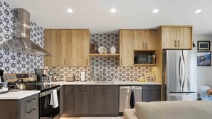 Een moderne keuken met houten kastjes, een roestvrijstalen afzuigkap, een magnetron en een koelkast.