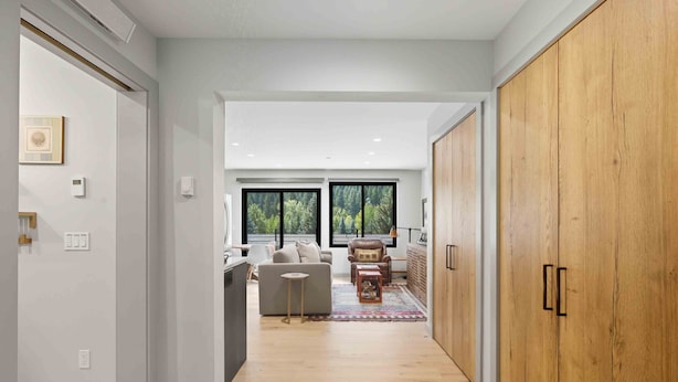 Een modern interieur met een houten garderobe, een grijze bank en een eethoek met een tafel en stoelen.