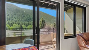 Een balkon met uitzicht op een bebost gebergte, een tafel met een kleurrijk tafelkleed en een lederen stoel.