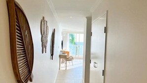A hallway with a large wooden decorative piece on the left, a door on the right, and a view into a room with a table and chairs. - Amazing Water View Apartment - Pool, Gym, Parking. (Urangan)