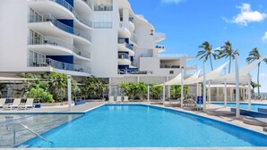 A modern hotel with a large pool, multiple balconies, and palm trees. - Amazing Water View Apartment - Pool, Gym, Parking. (Urangan)
